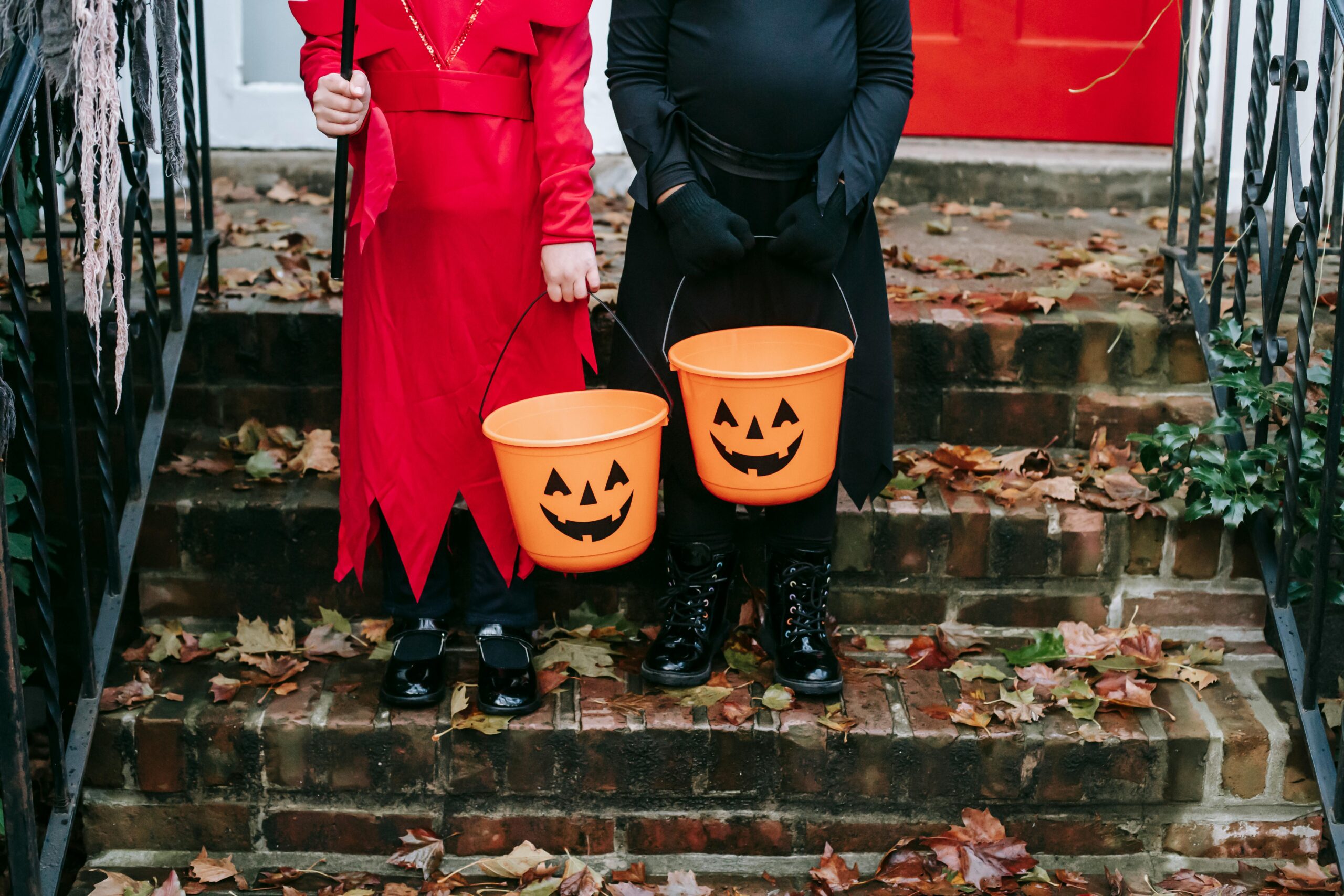 Two children in costumes holding pumpkin buckets, ready for Halloween trick-or-treating.